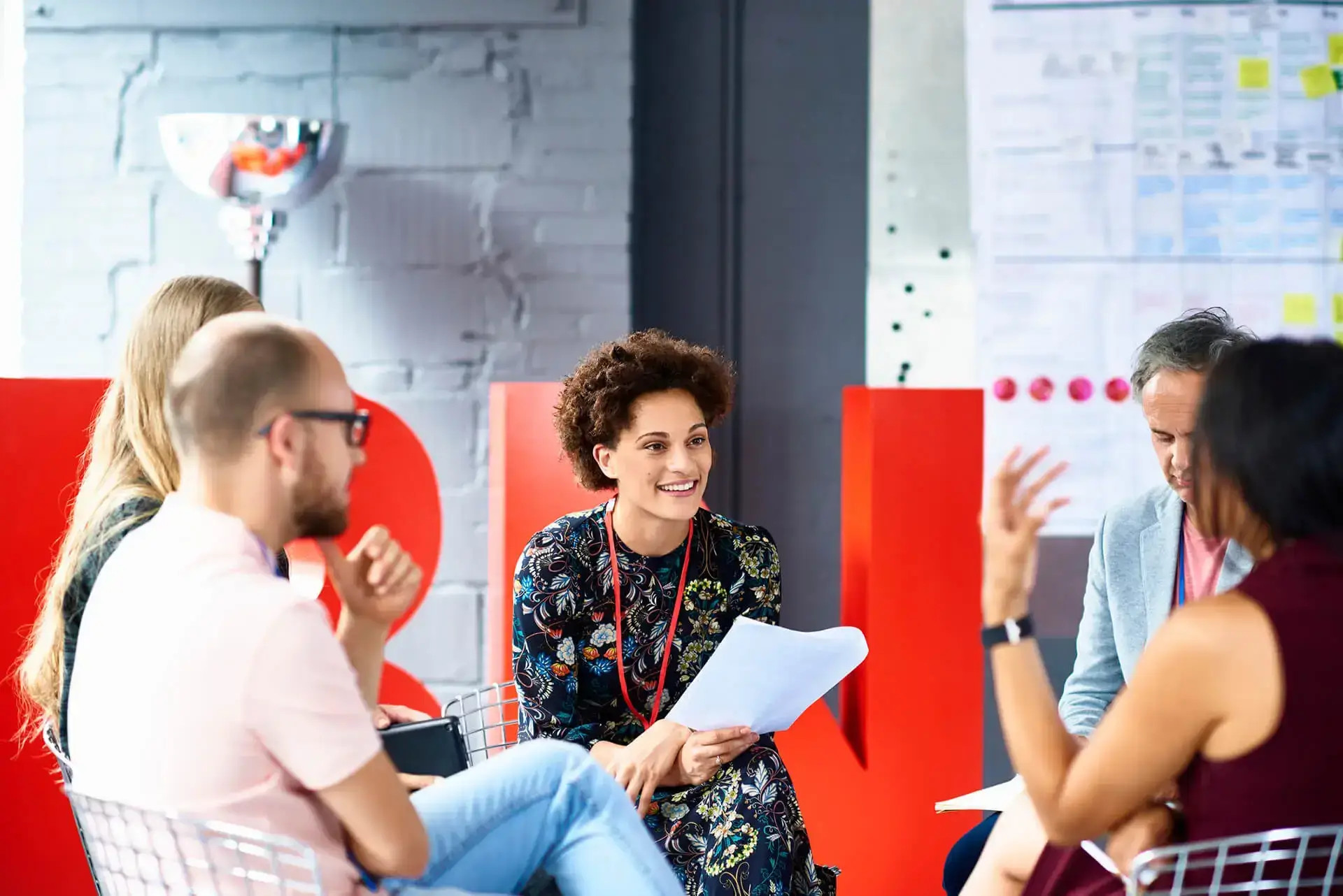 Mujer sonriente con credencial sostiene papeles mientras conversa con colegas en sala de reuniones moderna. Emprende en TerritorioAloe