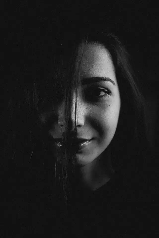 Retrato en blanco y negro de una mujer con mirada serena, iluminada desde un lado, fondo oscuro.