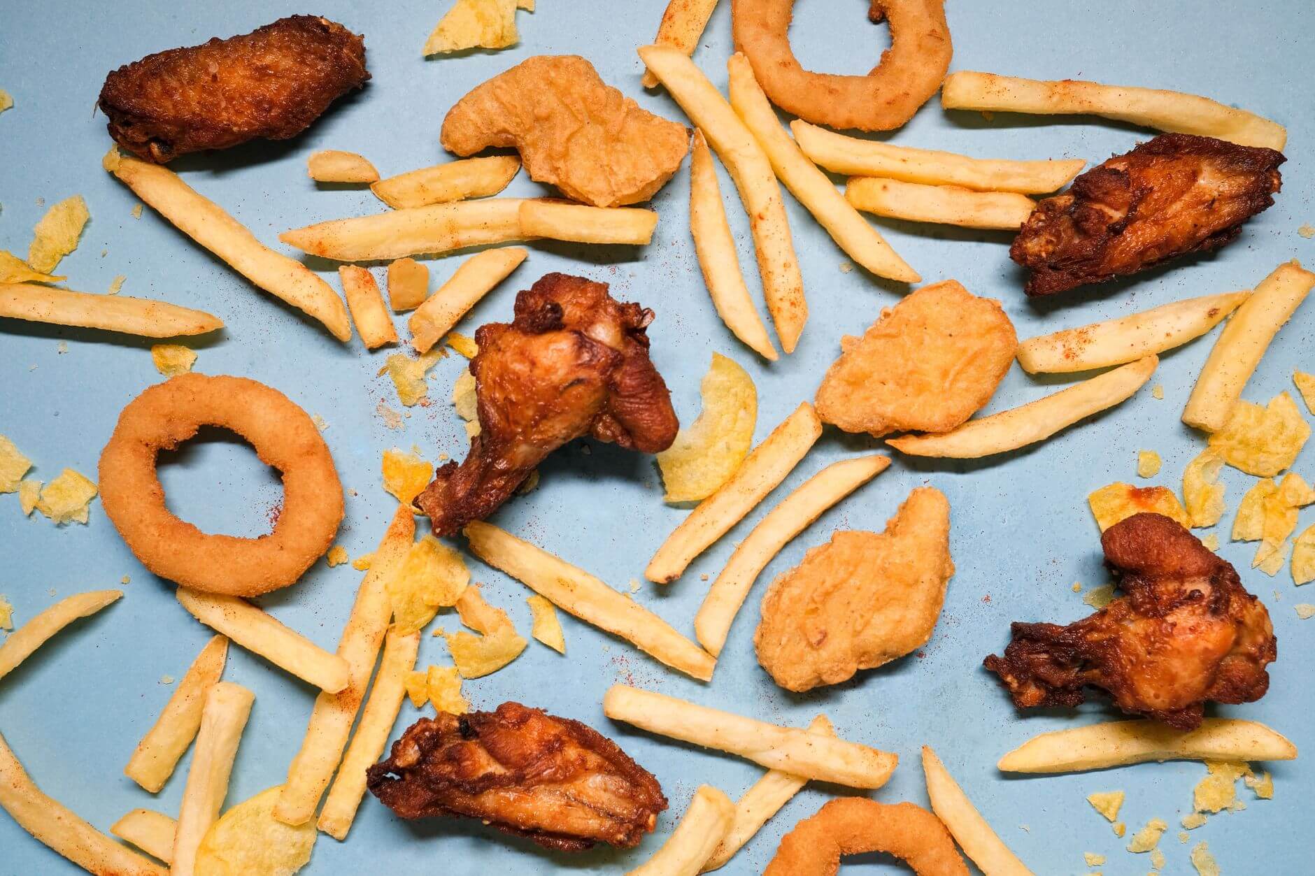 Papas fritas y trozos de pollo crujiente sobre bandeja azul, con bordes dorados y restos de especias. Grasas Saludables.
